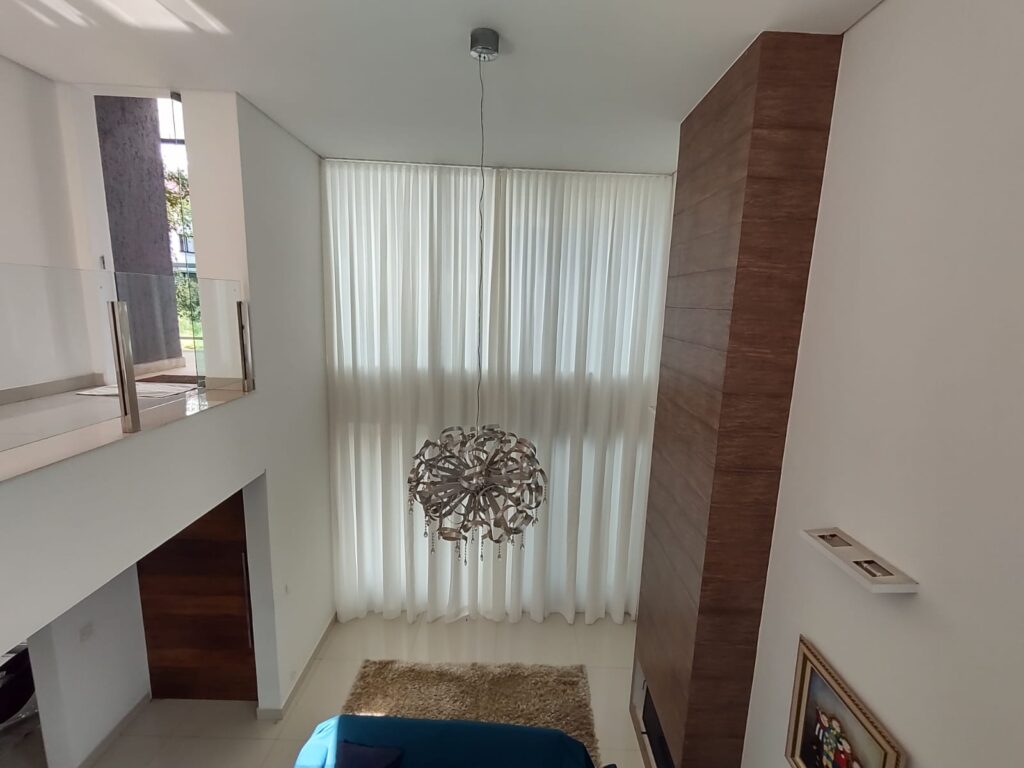 Cortina translúcida em sala com pé-direito duplo: a automação permite controlar a entrada de luz com um comando.